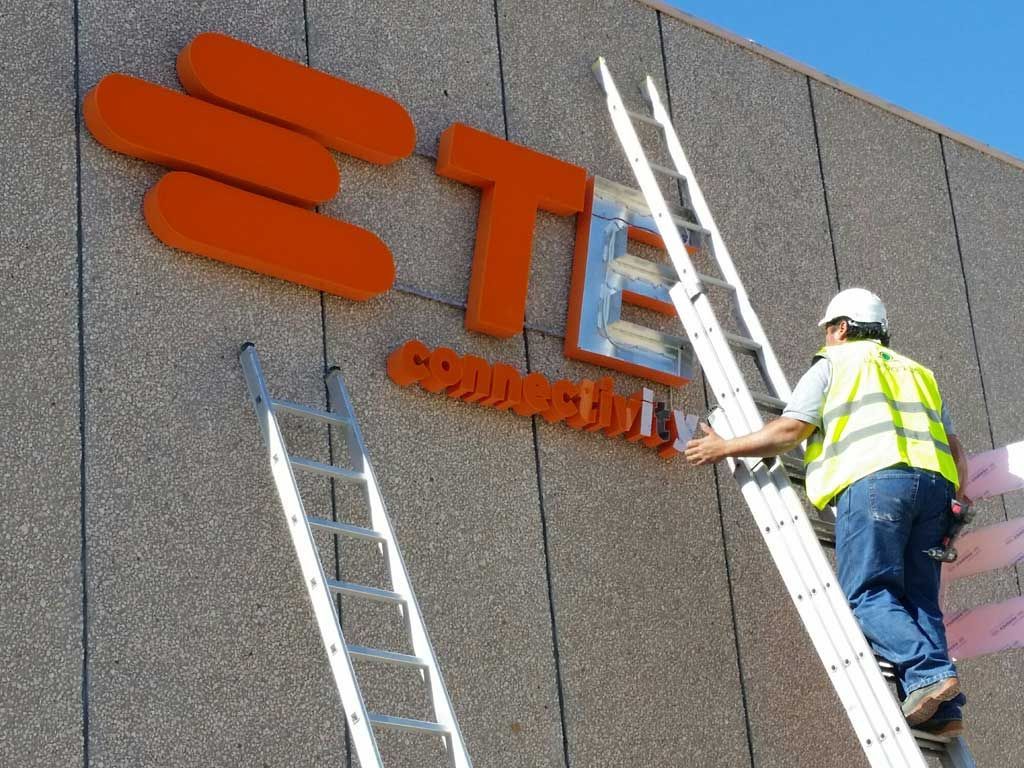 Um homem está em pé em uma escada consertando uma placa que diz ste