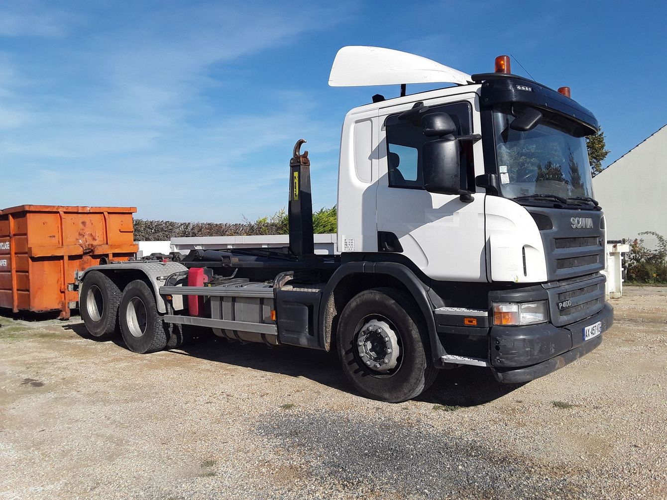 Camion blanc à bras articulé avec conteneur orange.