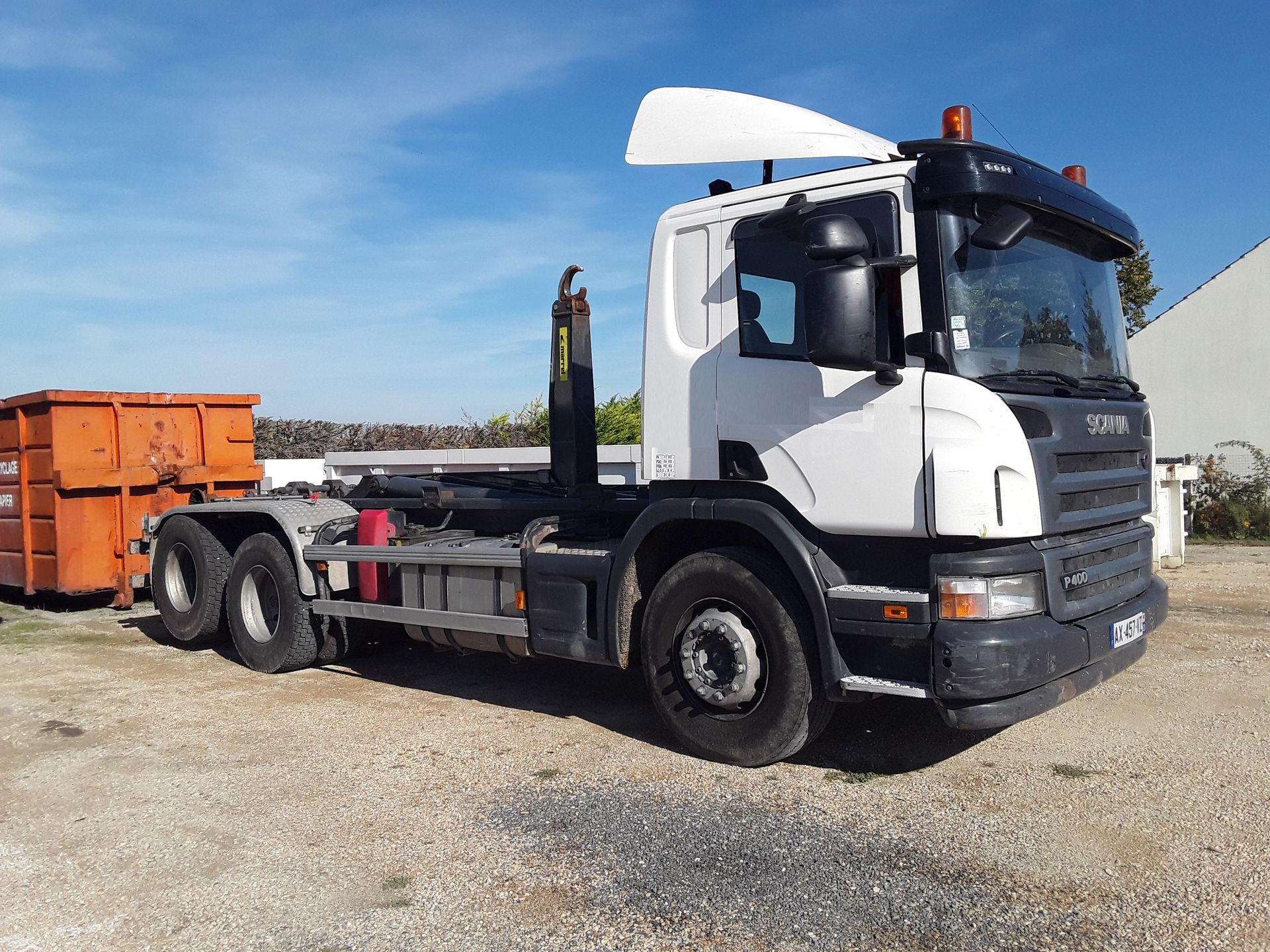Camion blanc à bras articulé avec conteneur orange.