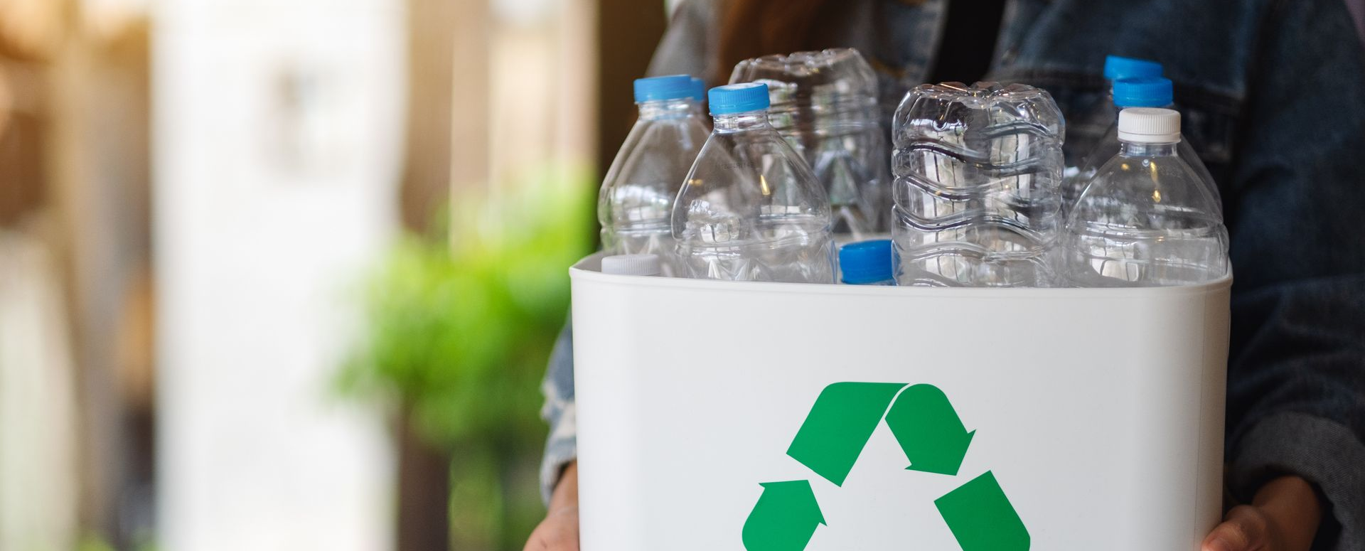 Une personne tenant une poubelle de recyclage blanche remplie de bouteilles d'eau en plastique.