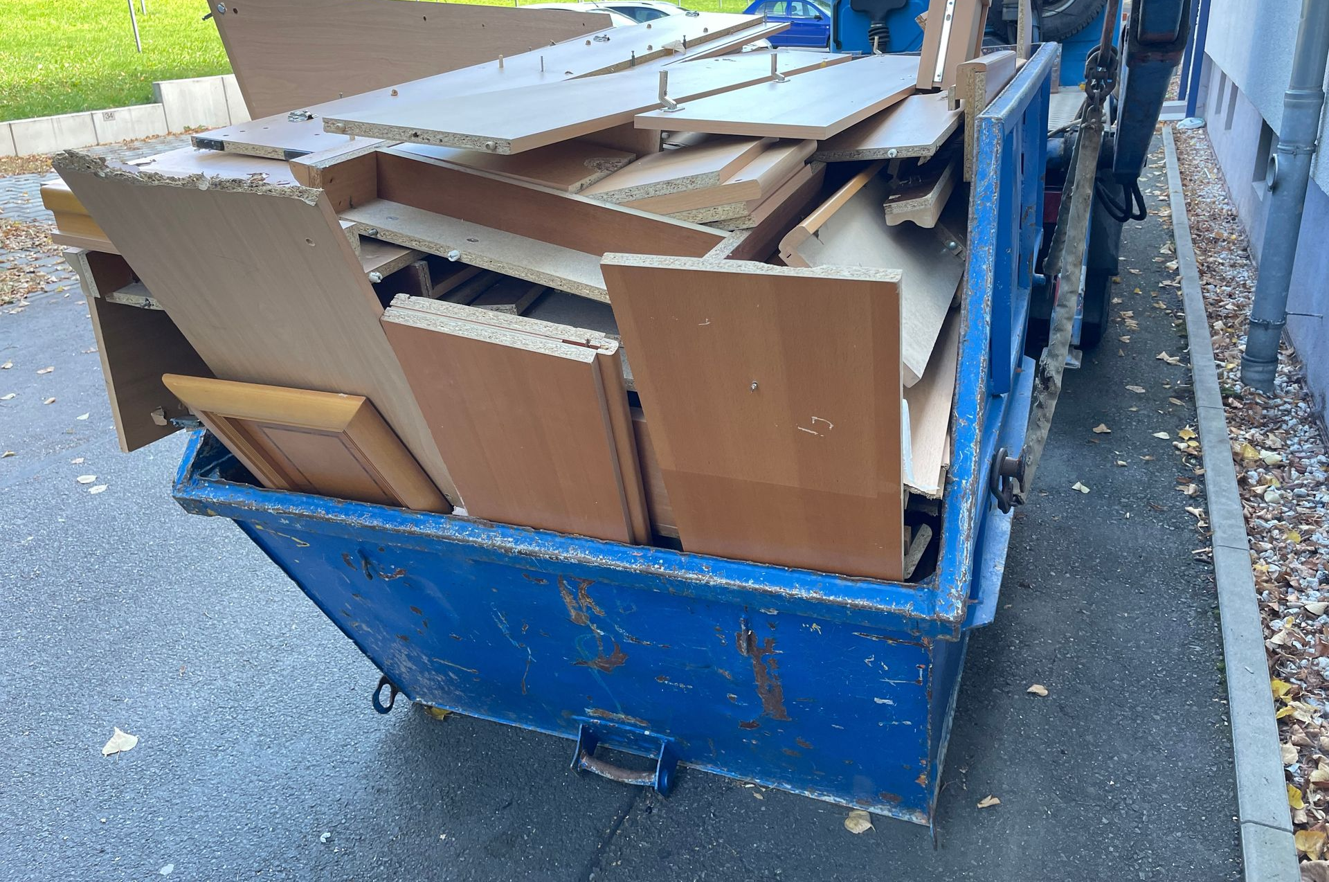 Une benne bleue remplie de déchets de meubles en bois.