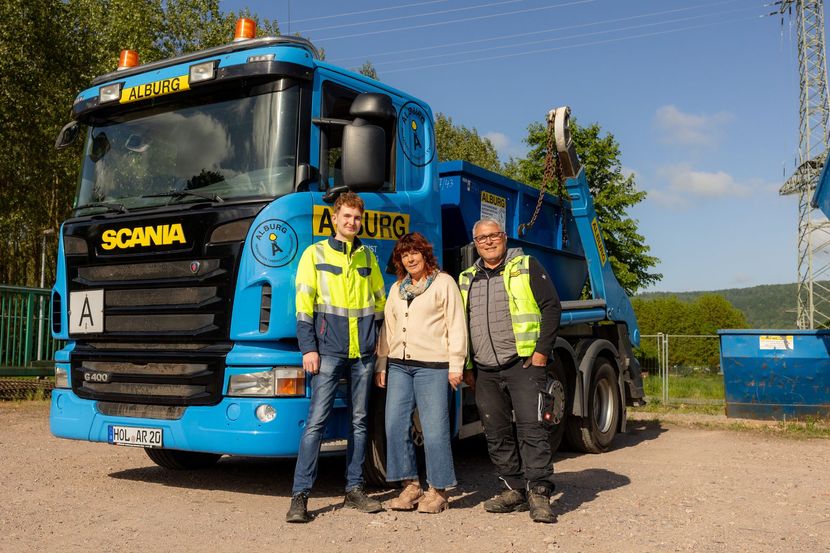 Drei Personen stehen vor einem blauen Scania-Truck