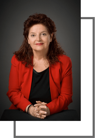 Mujer con blazer rojo, manos juntas, sonriendo. Fondo gris oscuro con marco blanco.