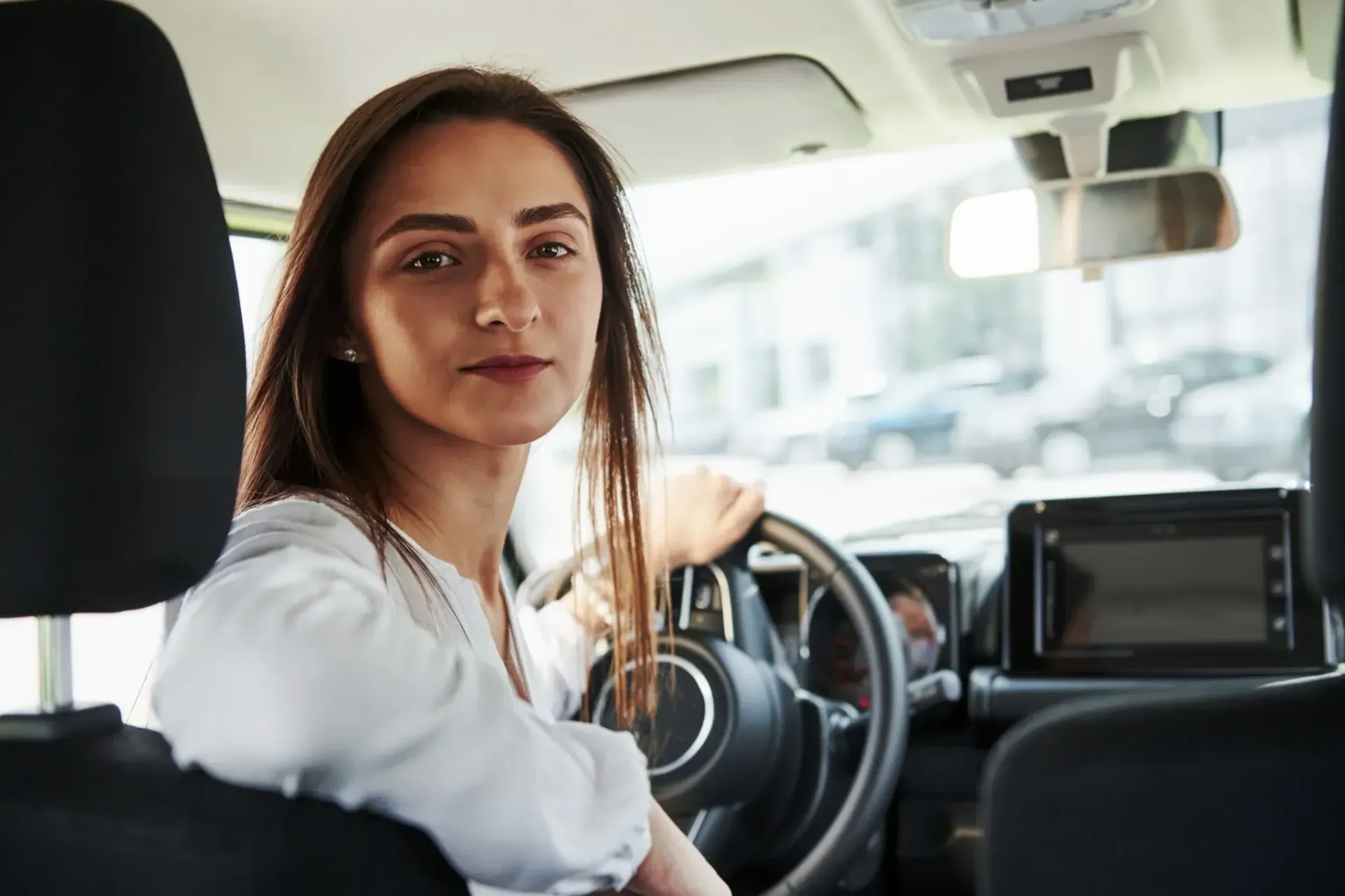 Mujer sentada al volante de un coche, mirando hacia la cámara.