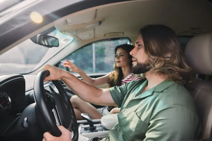 Hombre conduciendo un coche, mujer en el asiento del pasajero extendiendo la mano hacia la ventana, vista interior.