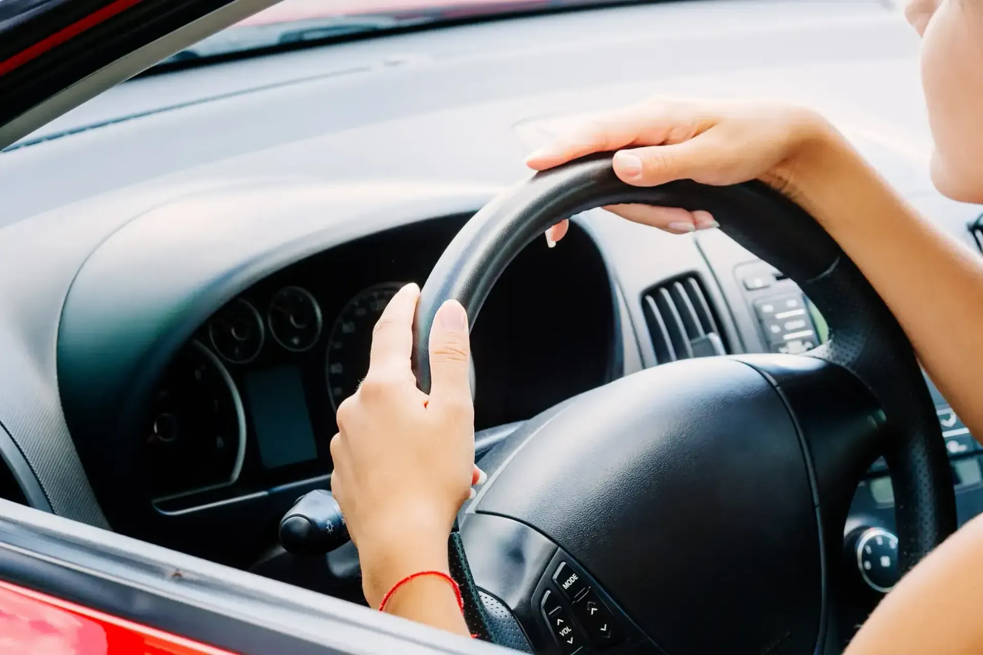Manos sobre un volante negro dentro de un coche rojo.