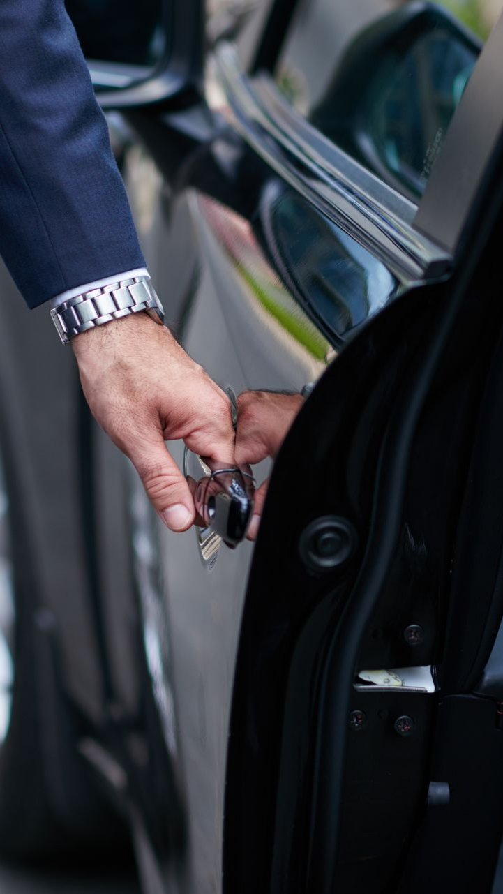 Un homme en costume ouvre la portière d'une voiture noire.