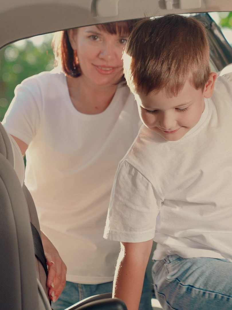 Une femme aide un enfant à monter dans la voiture.