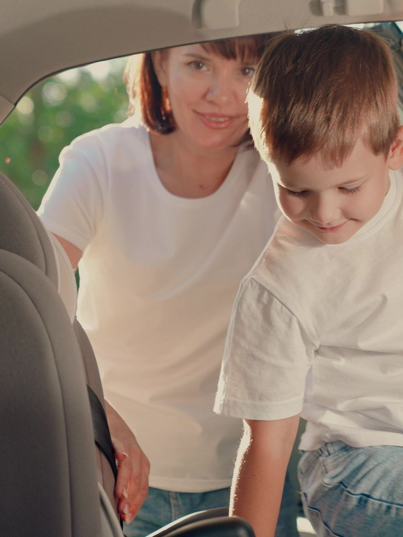 Une femme aide un enfant à s'installer dans la voiture.