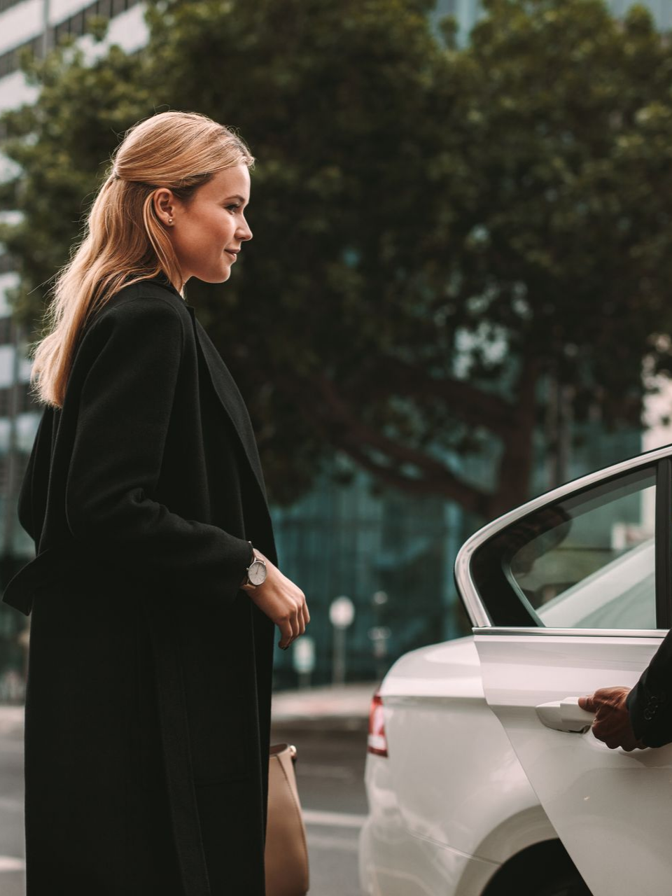 Une femme rentre dans une voiture blanche aidée par une personne qui lui ouvre la portière.