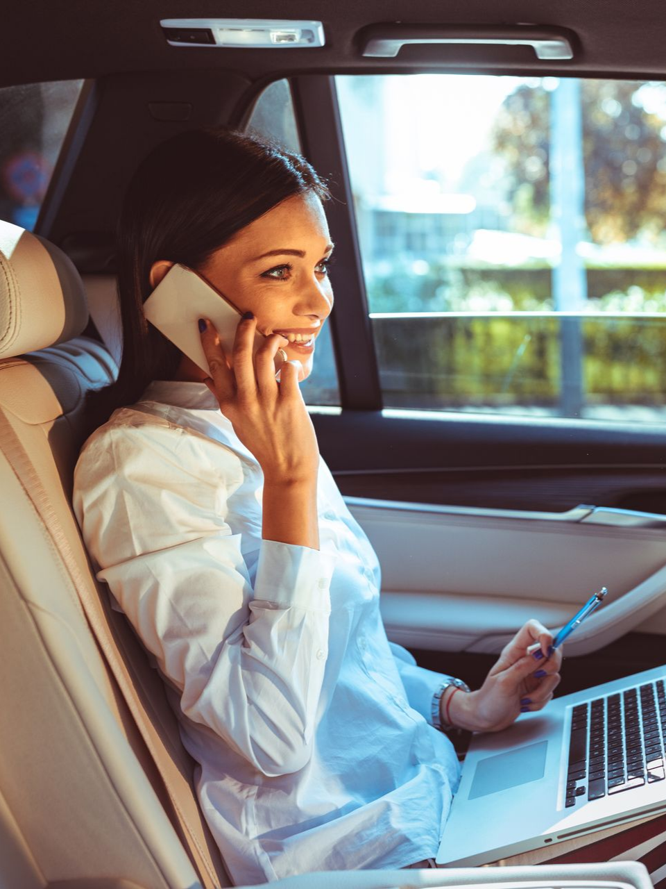 Femme en voiture, au téléphone travaillant sur son ordinateur portable.