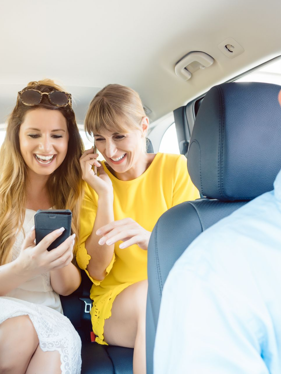 Deux femmes rient en regardant leur téléphone dans une voiture.