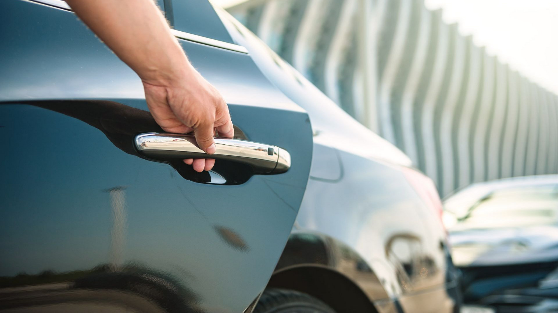Main ouvrant la poignée de la portière d'une voiture noire.