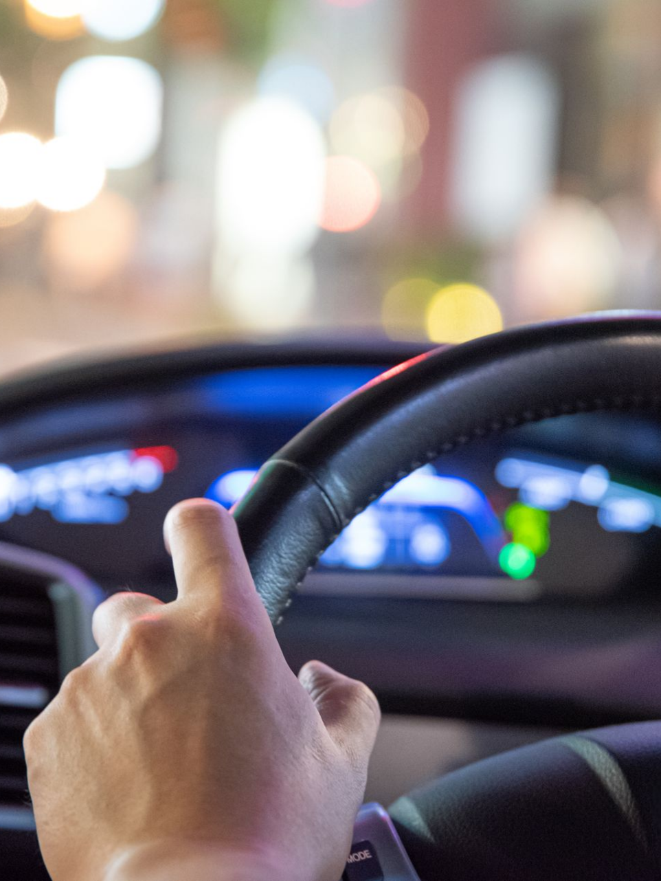 Une main tenant un volant noir, conduisant de nuit.