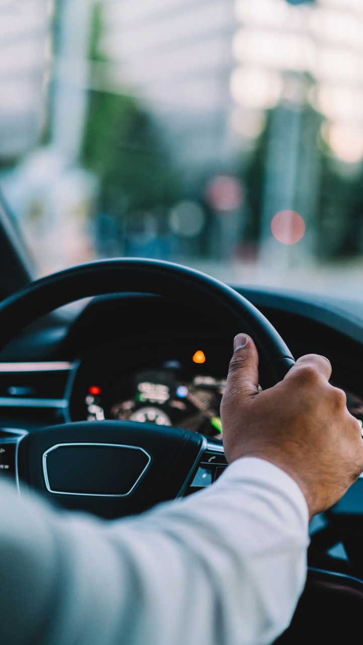 Une main posée sur un volant noir, au volant d'une voiture.