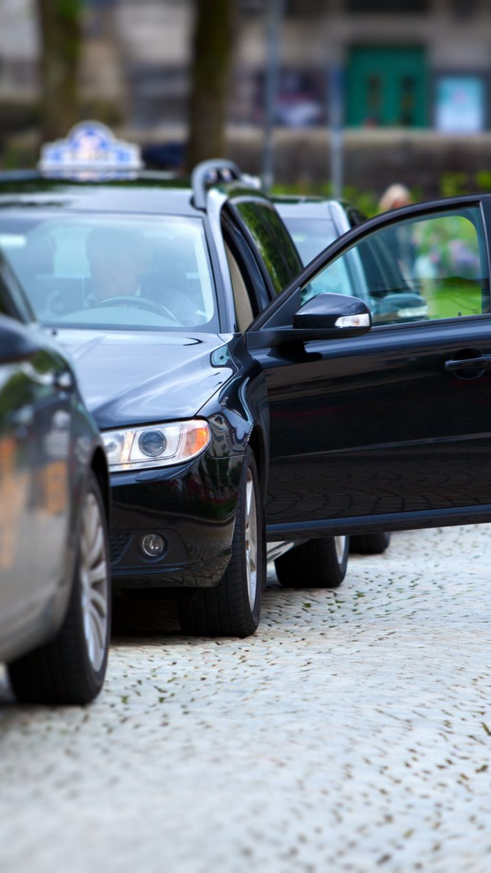 Taxi noir, portière ouverte, stationné dans une rue pavée.