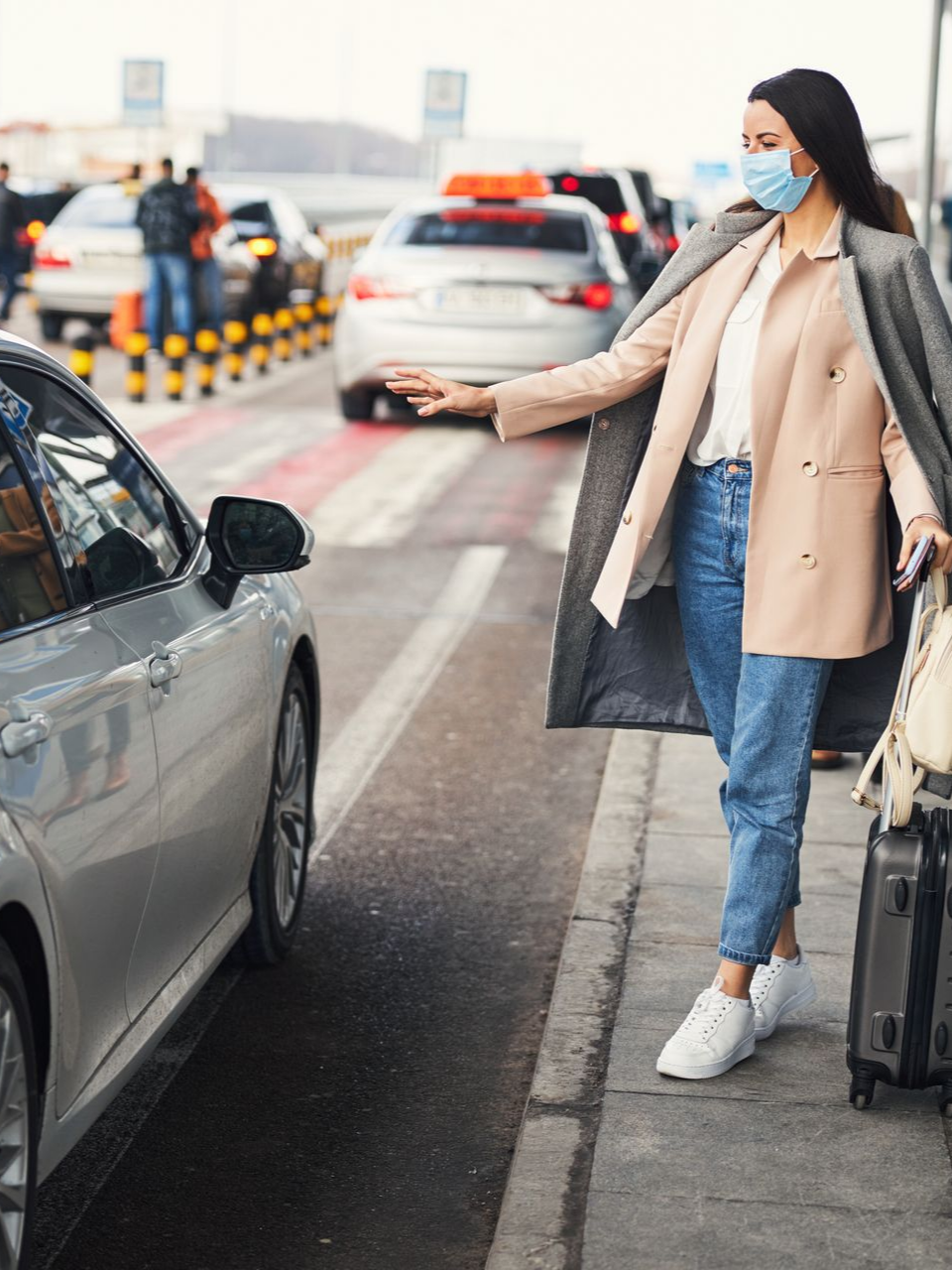 Une femme appelle un taxi au bord du trottoir d'un aéroport.
