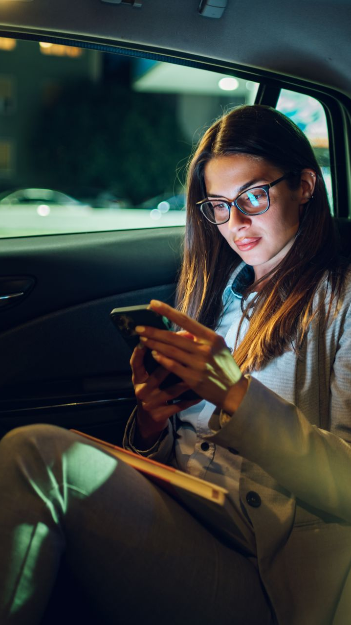 Une femme dans une voiture, la nuit, regardant son téléphone.