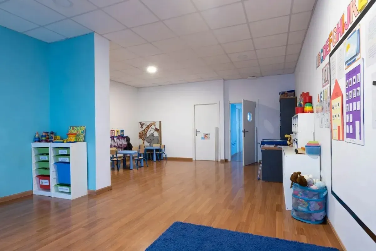 Aula vacía con paredes azules y blancas, piso de madera y estantes de almacenamiento coloridos.