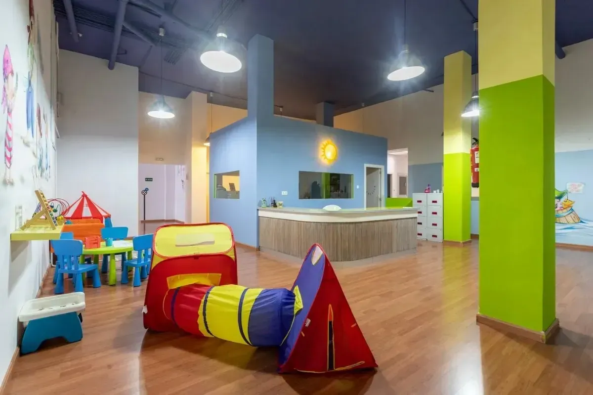 Interior de sala de juegos con túnel colorido, mostrador de recepción y muebles infantiles.