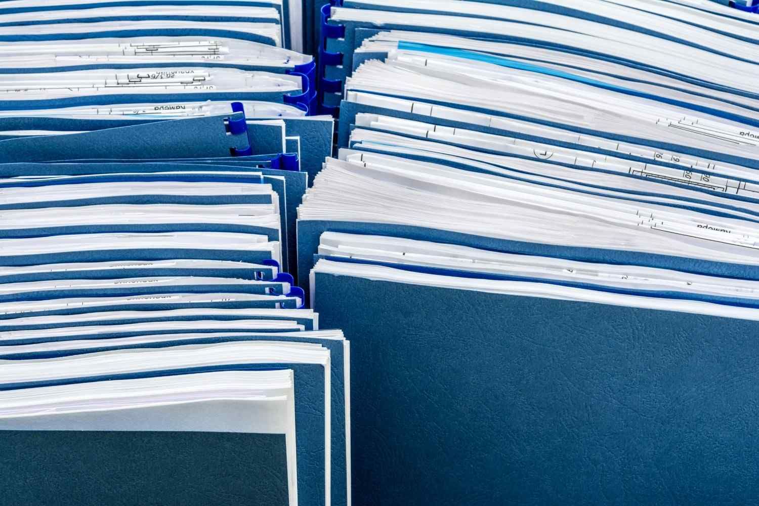 Pila de carpetas azules con los bordes blancos de las hojas a la vista, ordenadas sobre un escritorio o estante.