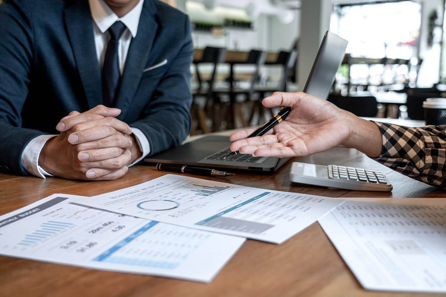 Reunión de negocios entre dos personas que analizan gráficos financieros en un escritorio con un portátil y un teclado