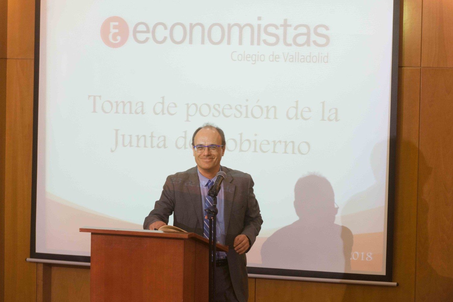 Un hombre habla desde un atril durante una presentación, con texto en español proyectado en la pantalla que tiene detrás.