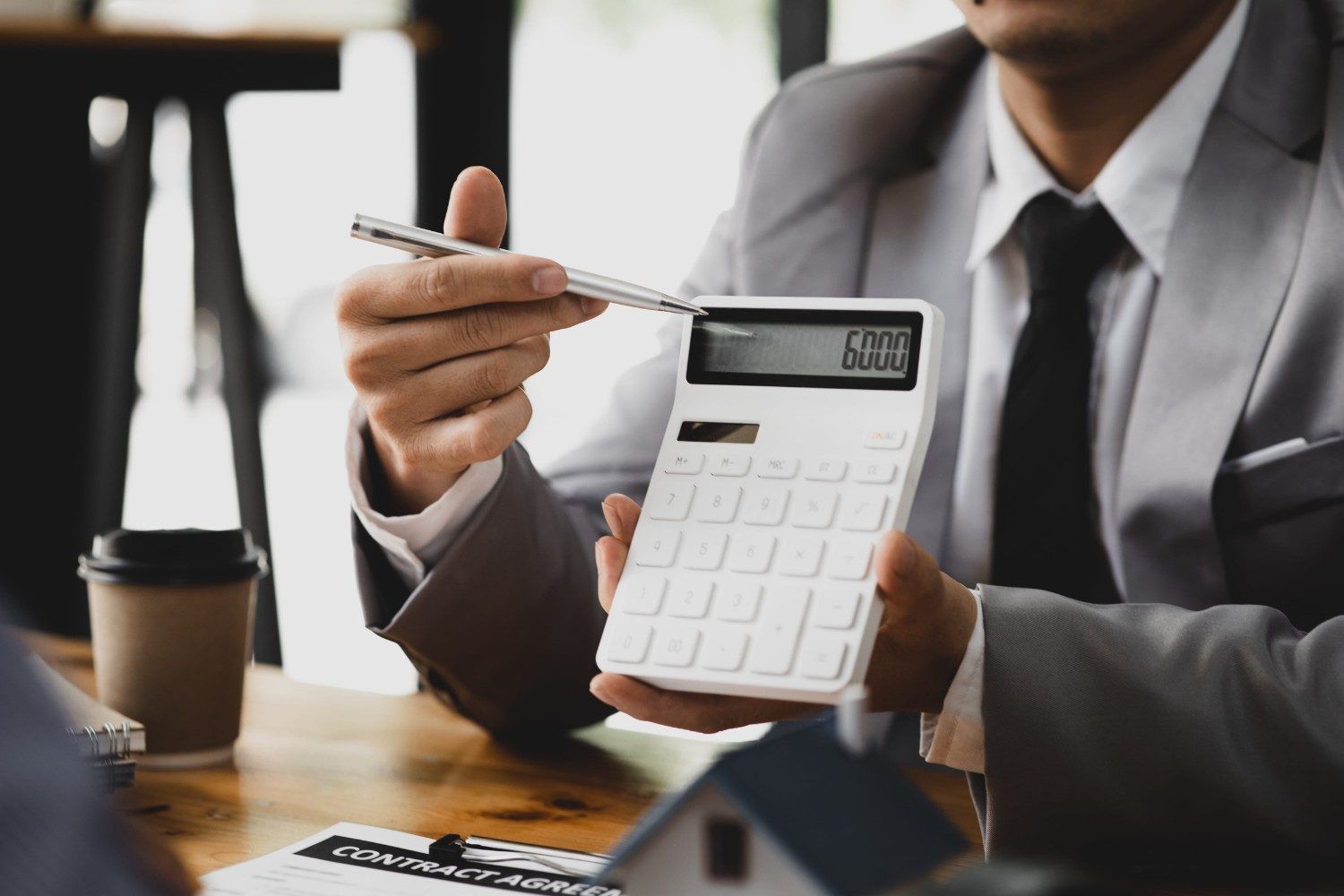Persona con traje, calculadora y bolígrafo en un escritorio con café, trabajando en sus finanzas