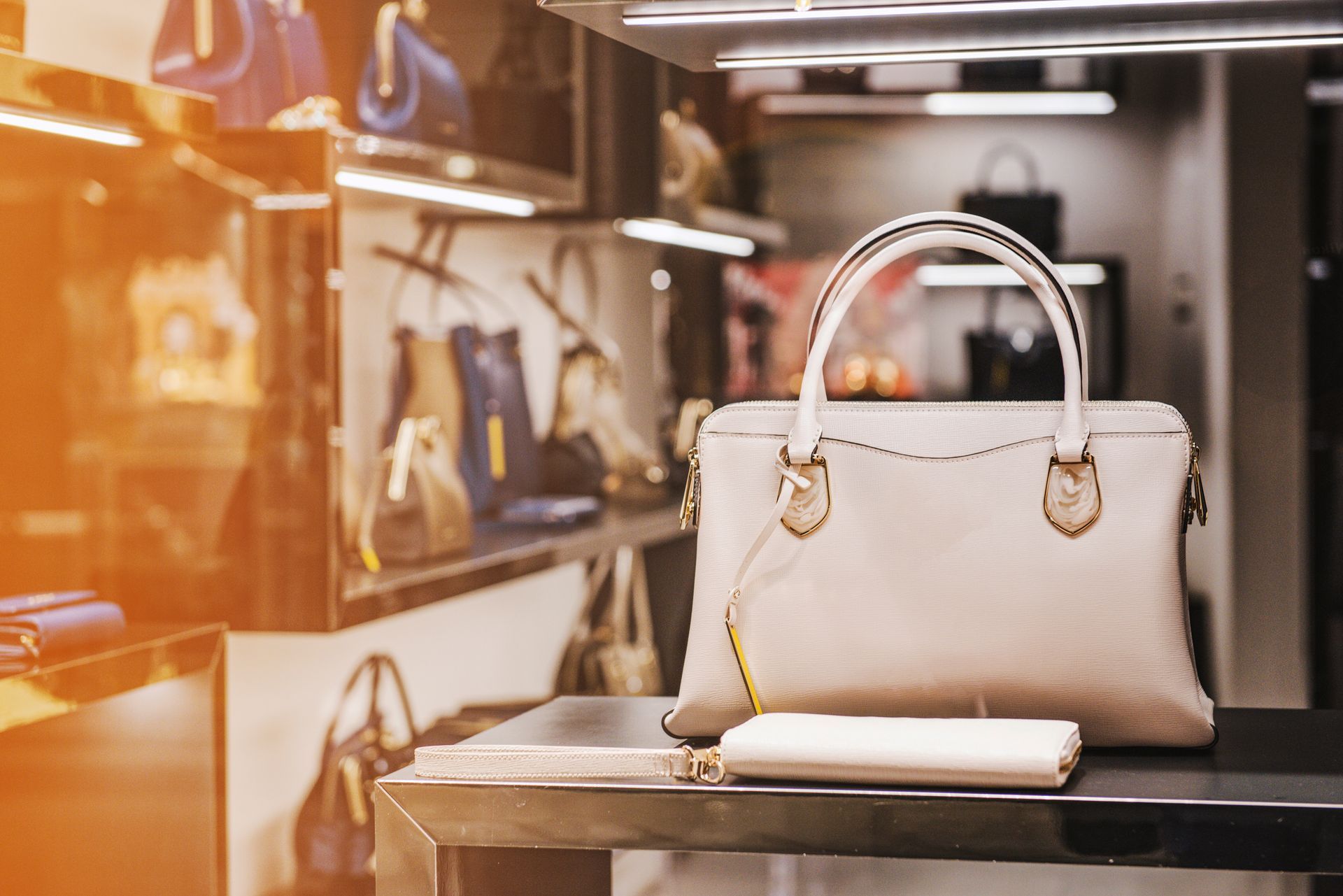Sac à main et portefeuille beiges présentés sur le comptoir d'un magasin éclairé d'une lumière chaude.