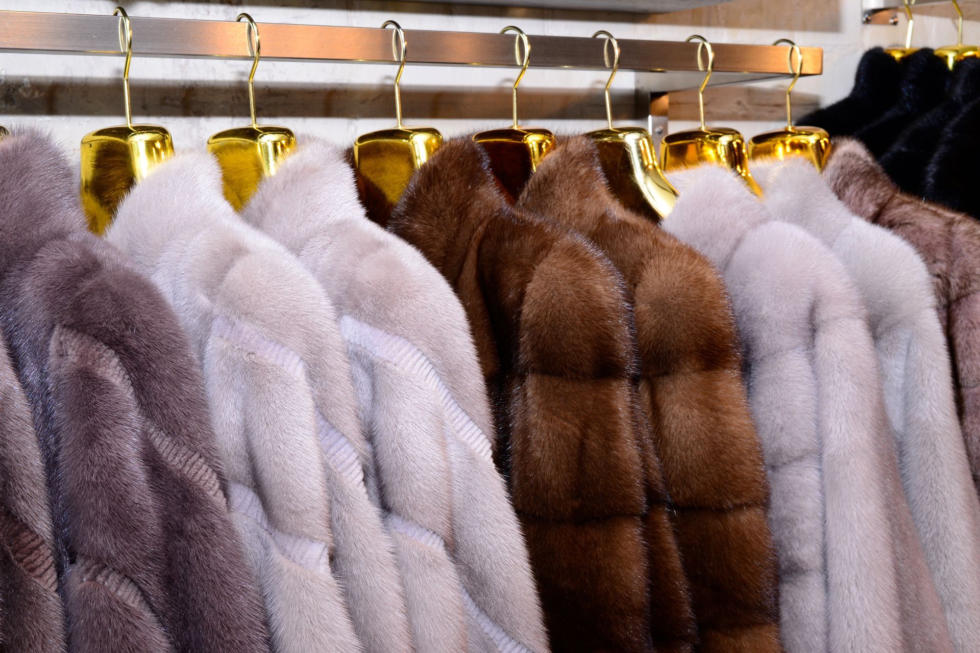 Des manteaux de fourrure blancs, beiges et marrons sont suspendus à des cintres dorés sur un portant.