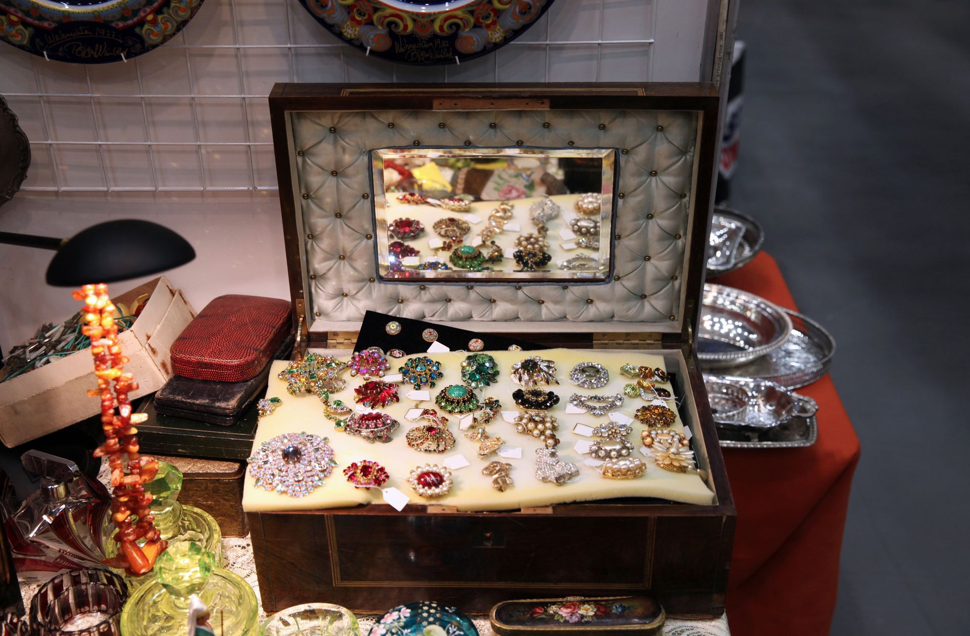 Vitrine à bijoux ouverte avec assortiment de bagues et de broches colorées sur une nappe rouge.