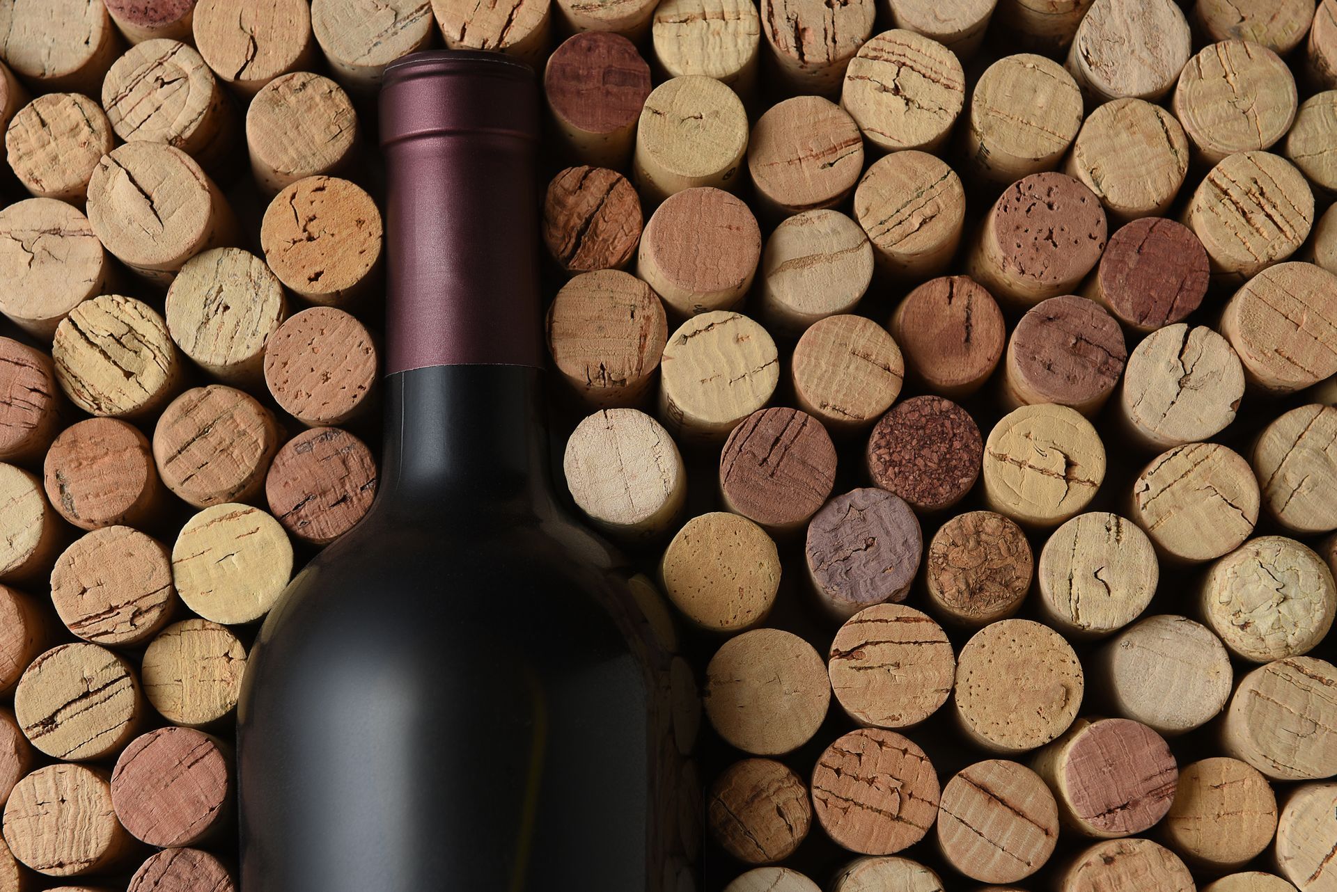 Bouteille de vin devant des bouchons empilés, avec un col bordeaux et un verre foncé.