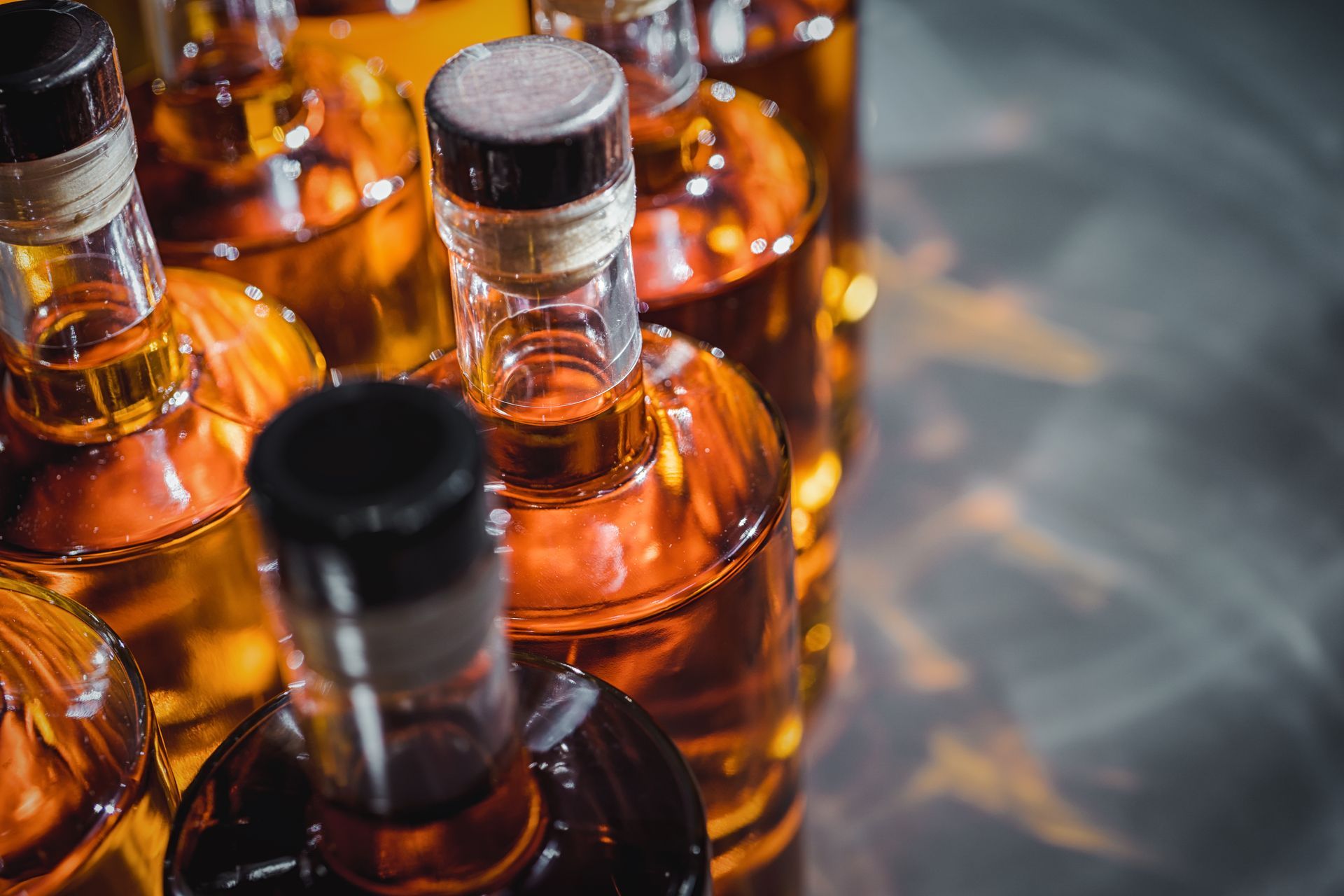 Bouteilles de liqueur ambrées à bouchons noirs disposées sur une surface réfléchissante.