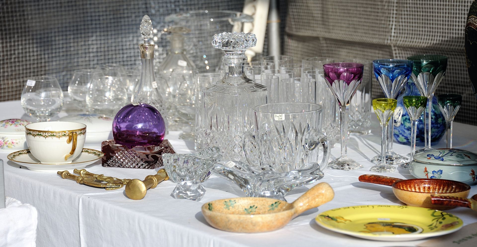 Table dressée avec un assortiment de verres, bols, tasses et assiettes, comprenant des verres à pied colorés et un bol violet.