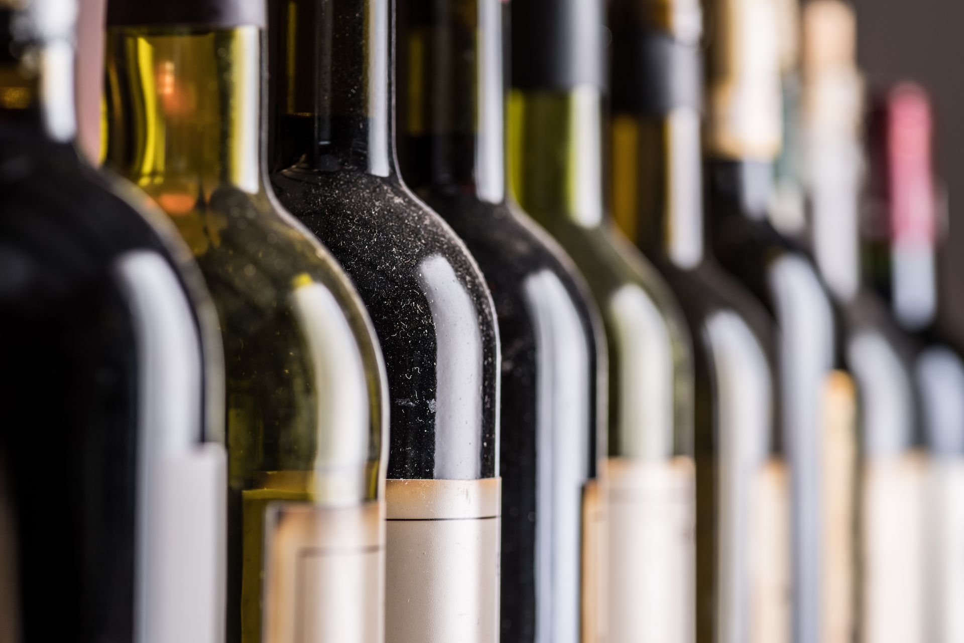 Rangée de bouteilles de vin sur une étagère, étiquettes et bouchons flous, dans un chai ou un magasin.