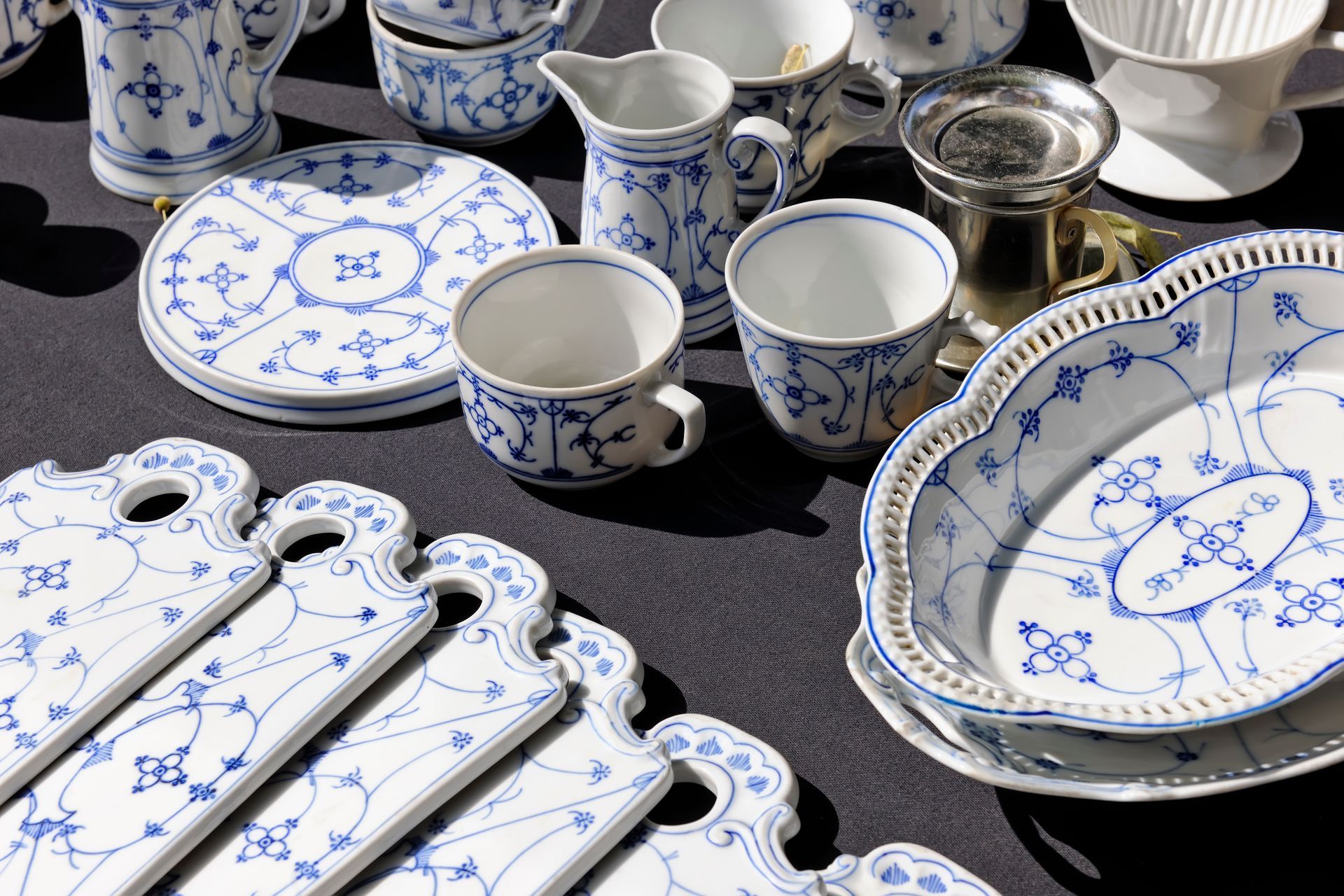 Service à thé en porcelaine bleue et blanche comprenant tasses, assiettes, théière et plateaux de service, sur une table sombre.