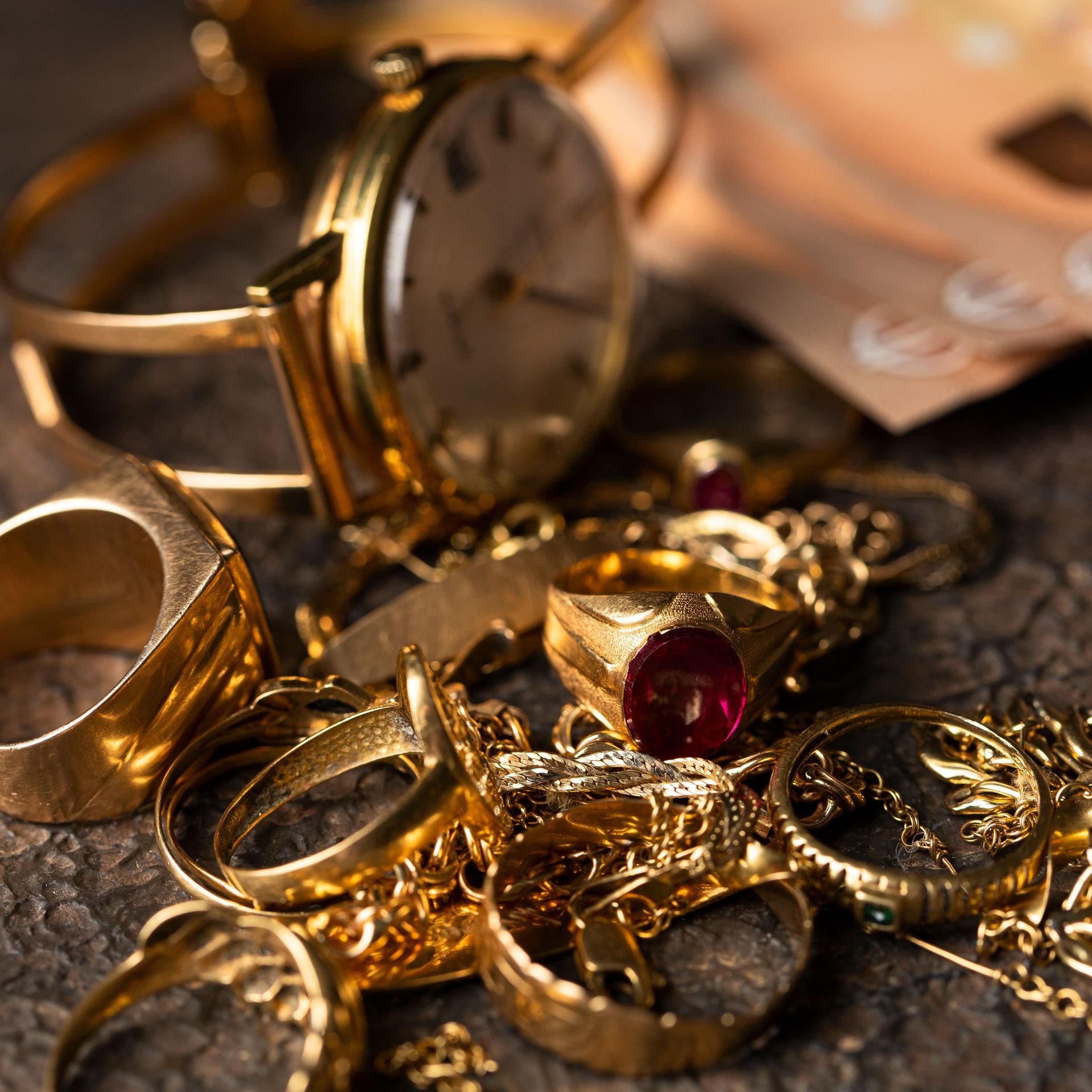 Des bagues en or et une montre de poche sont posées sur une surface sombre, avec une bague ornée de pierres précieuses au-dessus.