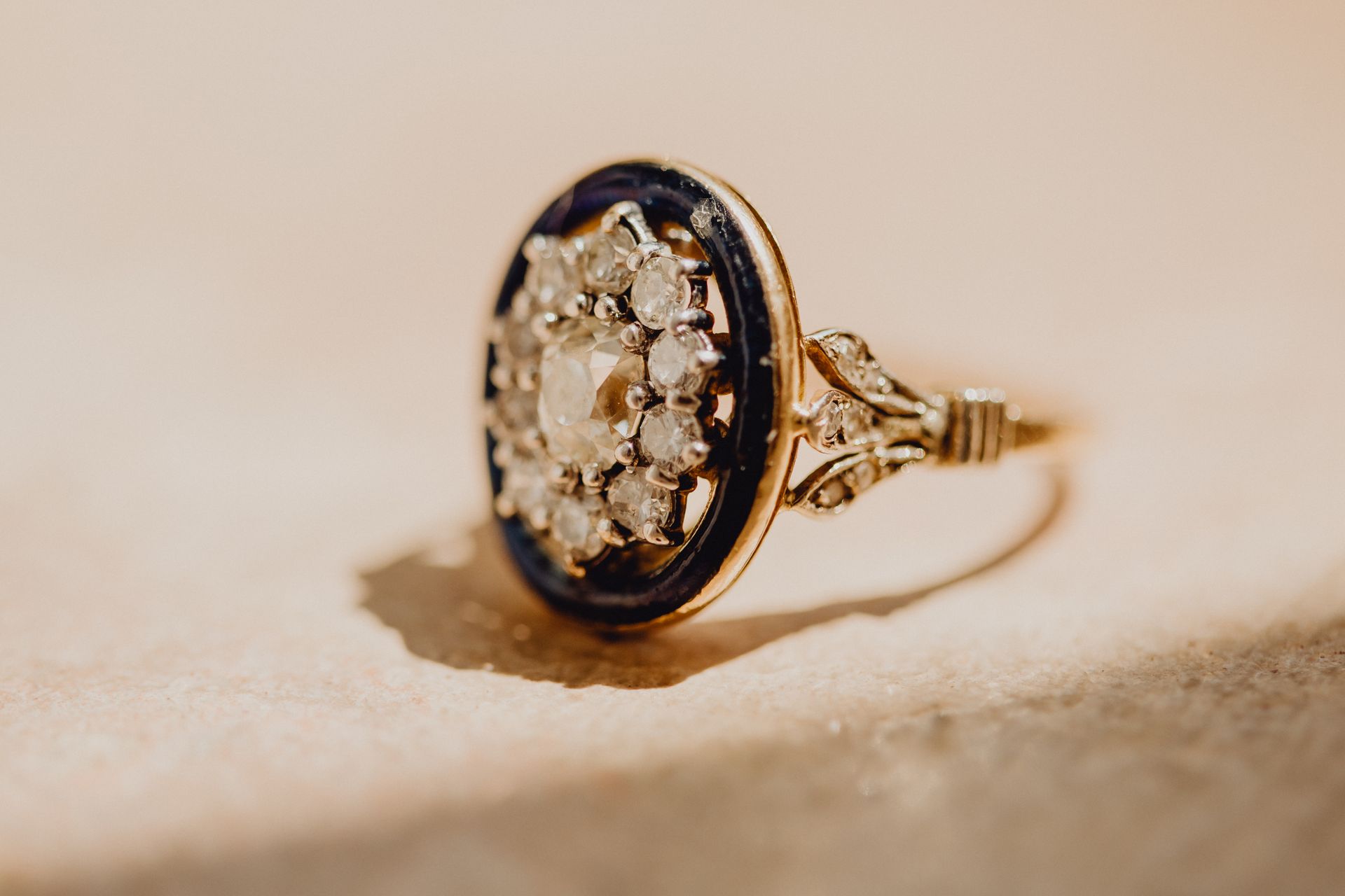 Bague ovale noire et or avec un motif floral groupé sur une surface beige.