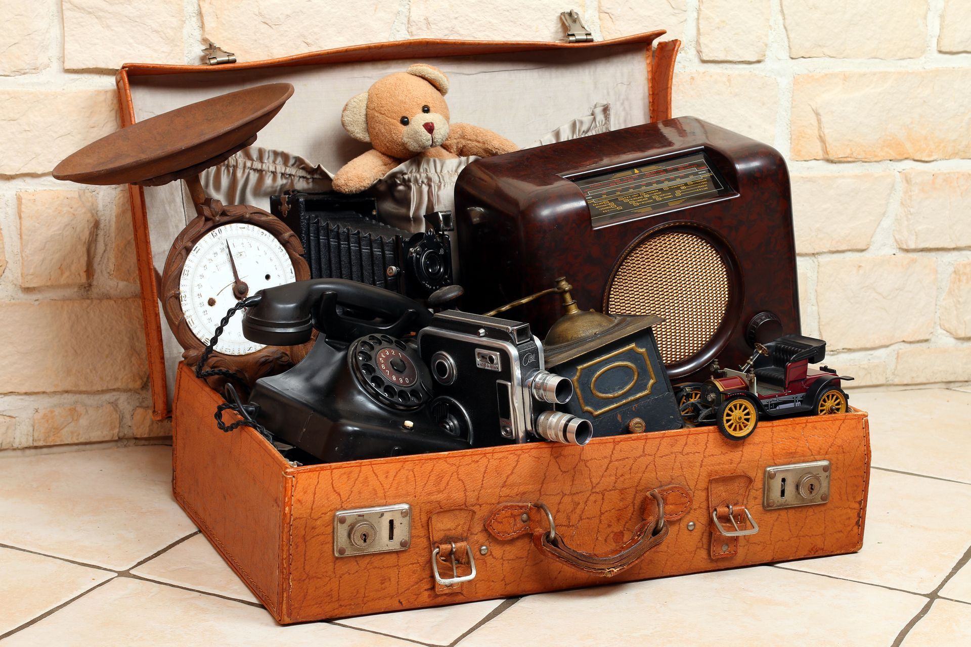 Valise ouverte remplie de radios vintage, d'un appareil photo, d'une horloge, d'un ours en peluche et d'objets anciens divers.
