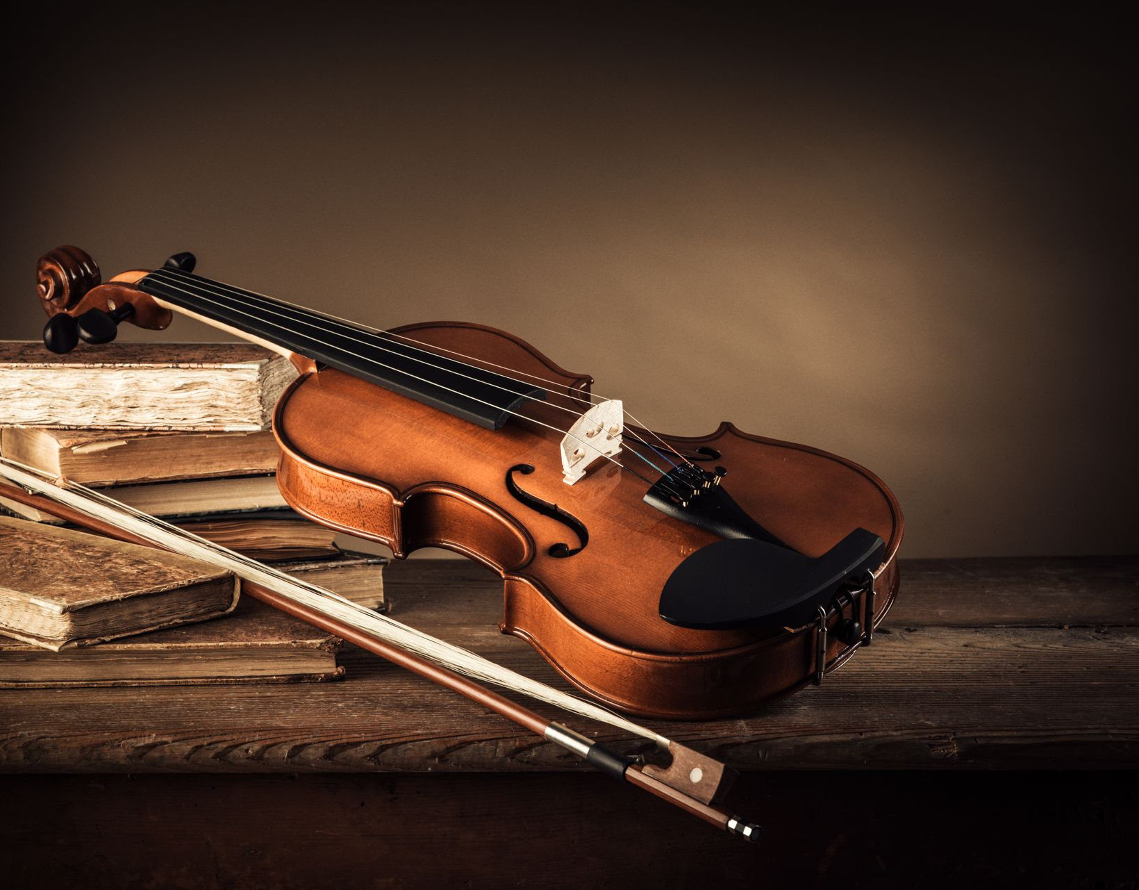 Violon et archet posés sur des livres empilés sur une table en bois rustique.