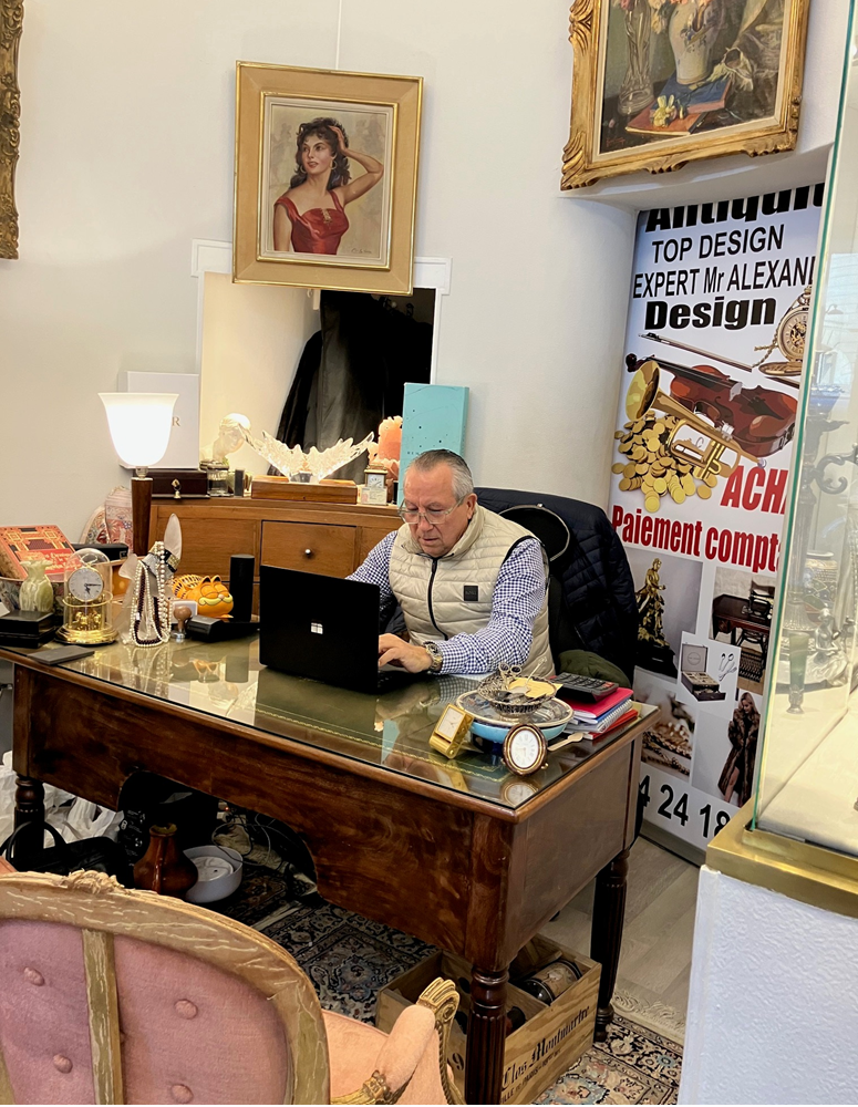 Un homme travaille sur un ordinateur portable à un bureau en bois dans un bureau décoré d'œuvres d'art, d'affiches et de portraits encadrés.