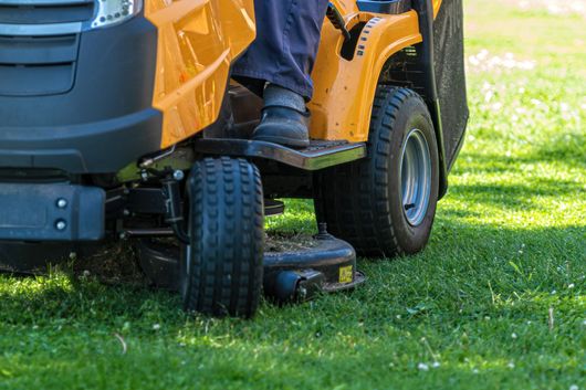 Une personne conduit une tondeuse à gazon orange sur de l'herbe verte, en train de tondre une pelouse.