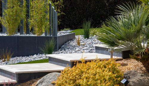 Jardin paysager moderne avec marches en pierre, gravier blanc et plantations de palmiers et d'arbustes.