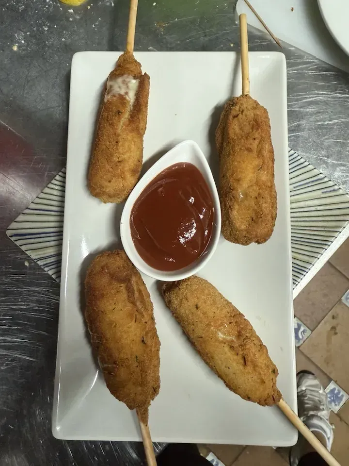 Perros de maíz en un plato rectangular blanco con un tazón pequeño de ketchup en el medio.