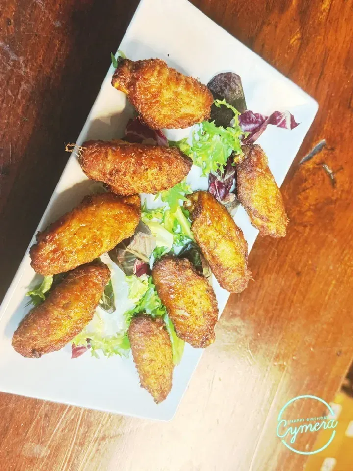 Alitas de pollo fritas doradas sobre un lecho de verduras, dispuestas en un plato rectangular blanco.