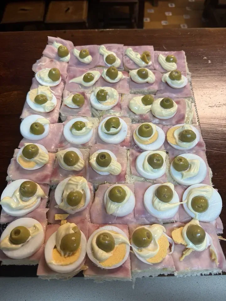 Sándwiches de jamón y huevo cubiertos con aceitunas dispuestas sobre una superficie de madera.