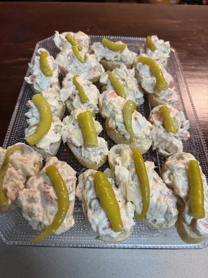Bandeja de aperitivos de ensalada de patatas sobre pan redondo, coronados con un pimiento encurtido.