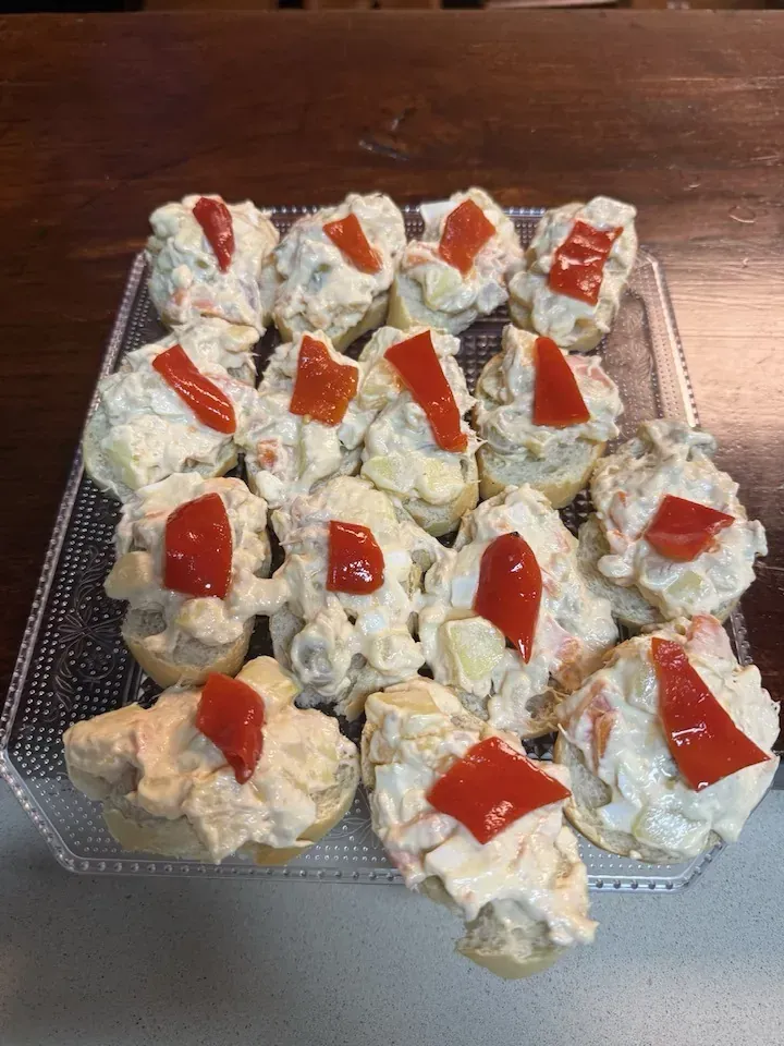 Bandeja de aperitivos de ensalada de patatas, cada uno cubierto con un cuadrado de pimiento rojo.