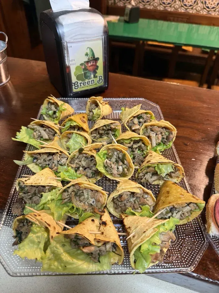 Bandeja de tacos pequeños con relleno de carne, lechuga y tortillas sobre barra de madera.