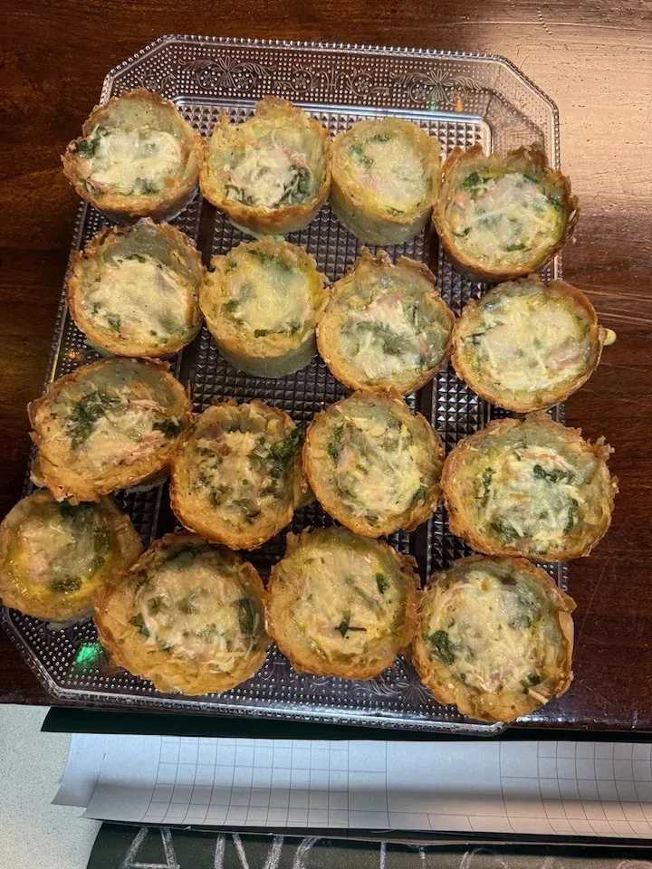 Bandeja de mini quiches saladas, horneadas y de color dorado con relleno verde visible